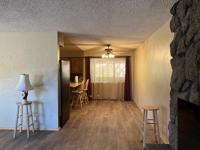 interior space with ceiling fan, a textured ceiling, a stone fireplace, wood finished floors, and baseboards