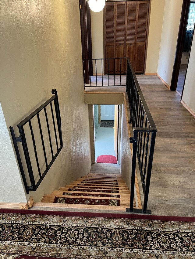 staircase featuring a textured wall, baseboards, and wood finished floors