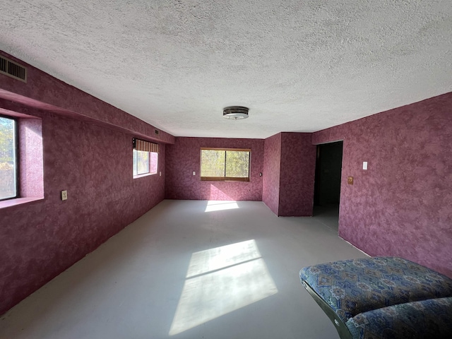 interior space with a textured ceiling, concrete floors, and visible vents