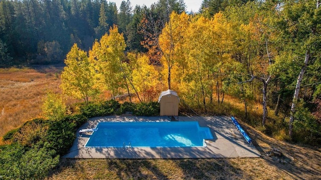 view of pool featuring a wooded view, an outbuilding, and a storage unit