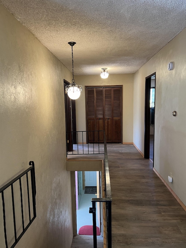corridor with a textured wall, a textured ceiling, an inviting chandelier, and wood finished floors