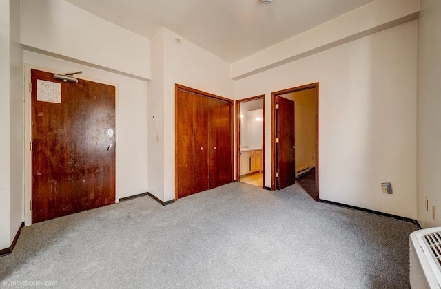 unfurnished bedroom featuring baseboard heating, light carpet, a closet, and ensuite bath