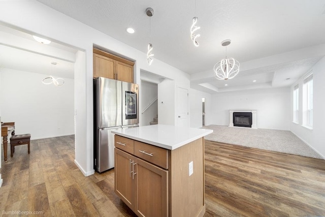 kitchen with stainless steel fridge, dark hardwood / wood-style flooring, a kitchen island, a tray ceiling, and decorative light fixtures