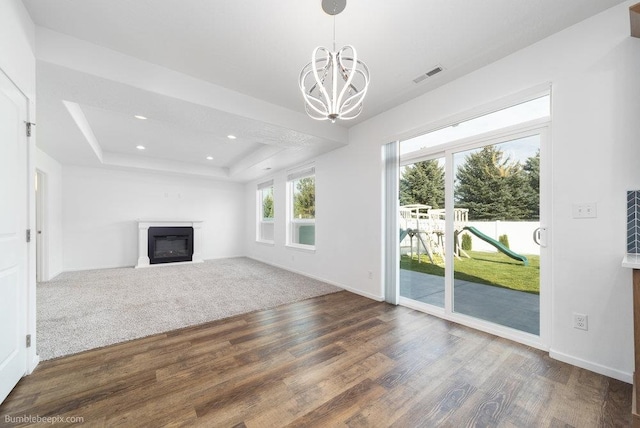 unfurnished living room with dark wood-type flooring, a notable chandelier, and a tray ceiling