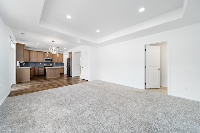 unfurnished living room with sink, hardwood / wood-style flooring, and a tray ceiling