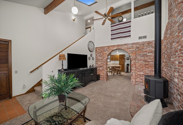 living room with beamed ceiling, ceiling fan, a towering ceiling, and a wood stove