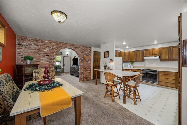 dining area with a textured ceiling, light colored carpet, and brick wall