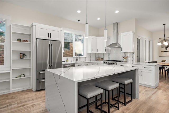 kitchen featuring a kitchen island, white cabinetry, wall chimney range hood, and stainless steel appliances