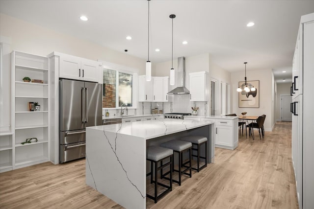 kitchen featuring high end refrigerator, a kitchen island, white cabinetry, light hardwood / wood-style flooring, and wall chimney exhaust hood