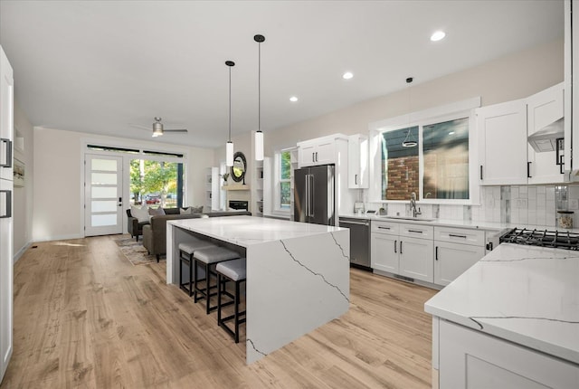 kitchen featuring light stone counters, appliances with stainless steel finishes, white cabinetry, light hardwood / wood-style floors, and a center island