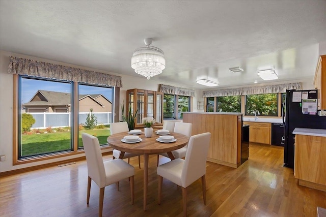 dining space featuring an inviting chandelier, light hardwood / wood-style floors, a textured ceiling, and a healthy amount of sunlight