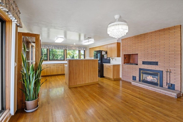 kitchen with a kitchen island, a textured ceiling, a brick fireplace, light hardwood / wood-style floors, and black refrigerator