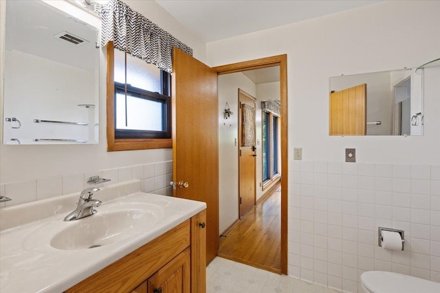 bathroom featuring vanity, toilet, wood-type flooring, and tile walls