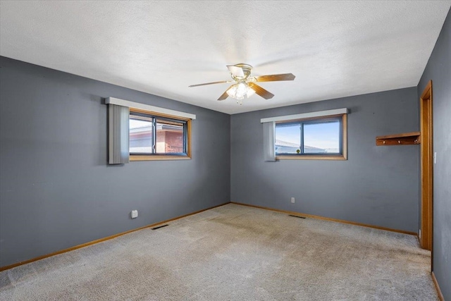 spare room featuring a wealth of natural light, a textured ceiling, light colored carpet, and ceiling fan