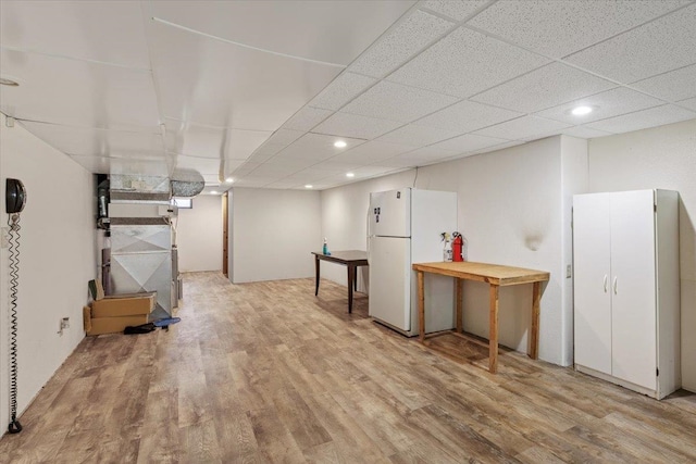 basement featuring a drop ceiling, light hardwood / wood-style flooring, and white refrigerator