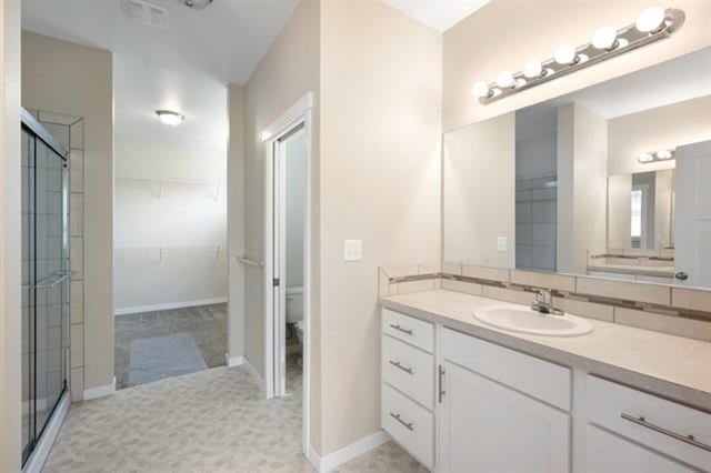 bathroom featuring a shower with door, vanity, toilet, and tile patterned floors