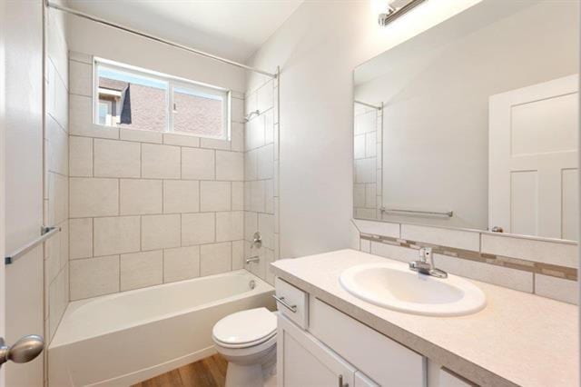 full bathroom with wood-type flooring, toilet, tiled shower / bath, vanity, and decorative backsplash