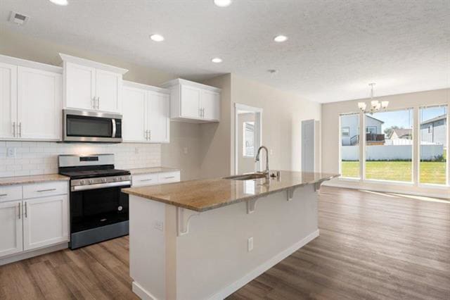 kitchen with white cabinetry, appliances with stainless steel finishes, sink, and a center island with sink