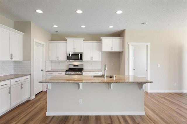 kitchen with hardwood / wood-style flooring, a center island with sink, sink, white cabinetry, and appliances with stainless steel finishes