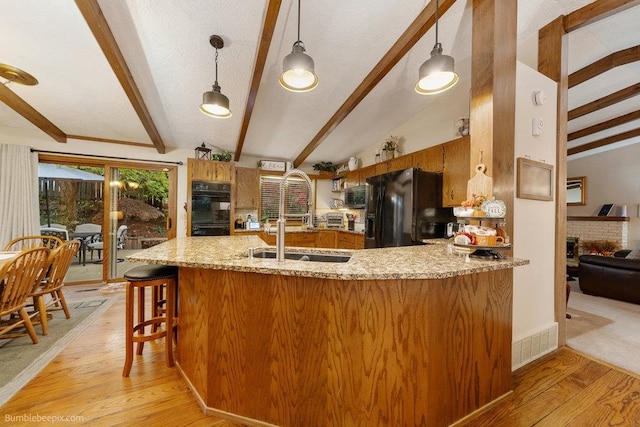 kitchen featuring vaulted ceiling with beams, kitchen peninsula, black appliances, decorative light fixtures, and light wood-type flooring