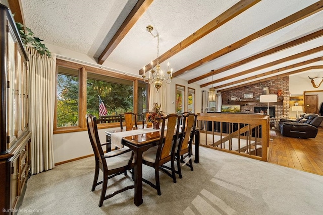 dining room featuring light hardwood / wood-style flooring, a brick fireplace, a textured ceiling, and lofted ceiling with beams