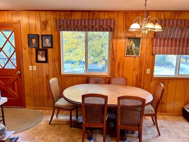 dining room with an inviting chandelier, wood walls, and a healthy amount of sunlight