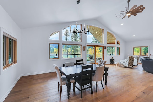 dining space with high vaulted ceiling, wood-type flooring, and ceiling fan with notable chandelier