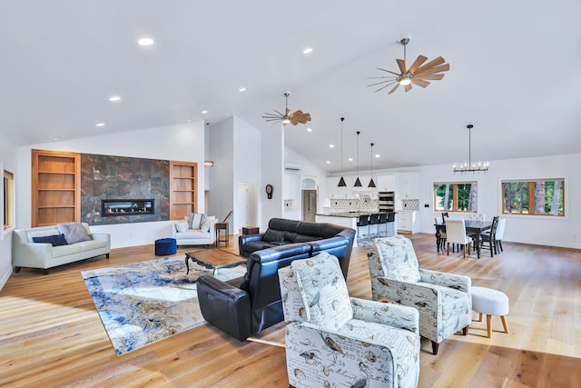 living room featuring high vaulted ceiling, a fireplace, light wood-type flooring, and ceiling fan with notable chandelier