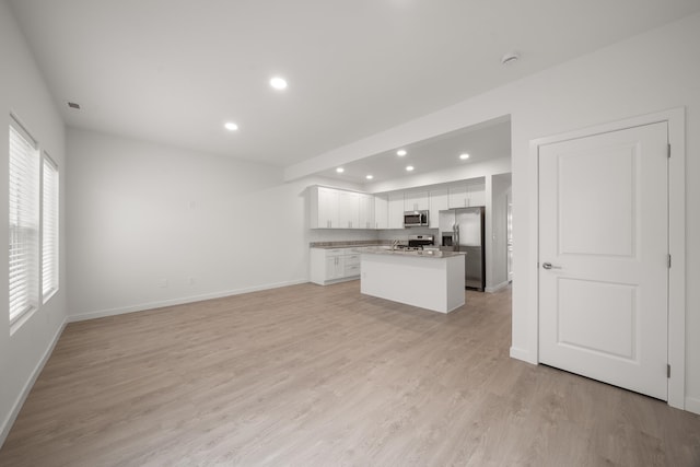 kitchen with stainless steel appliances, a center island, white cabinetry, light stone counters, and light hardwood / wood-style floors