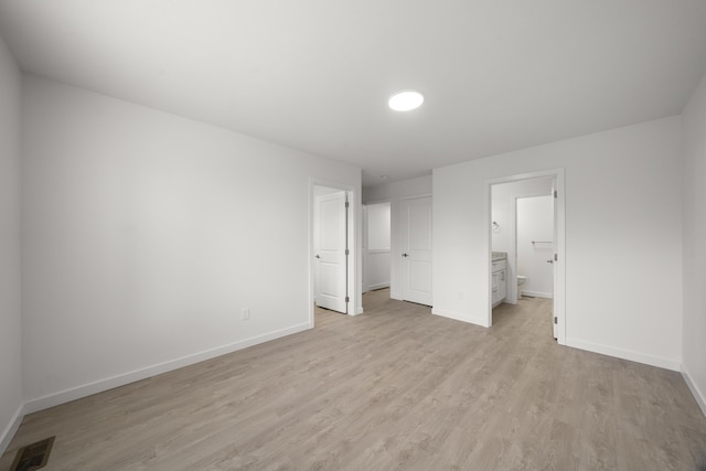 unfurnished bedroom with baseboards, ensuite bathroom, light wood finished floors, and visible vents