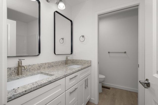 bathroom with a sink, toilet, wood finished floors, and visible vents