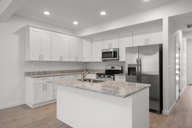 kitchen with white cabinetry, stainless steel appliances, light stone countertops, and a kitchen island with sink