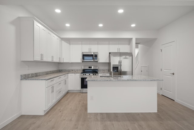 kitchen with light stone countertops, appliances with stainless steel finishes, a kitchen island with sink, and light wood-type flooring