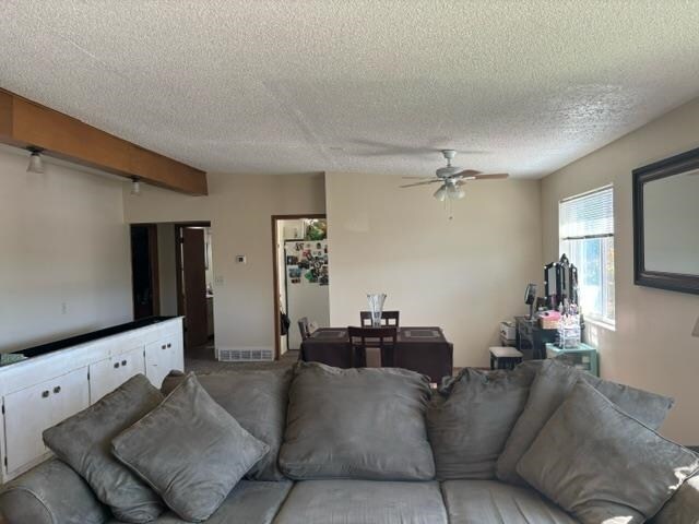 living room with beamed ceiling, a textured ceiling, and ceiling fan