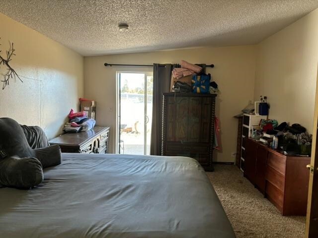 bedroom with a textured ceiling, carpet floors, and access to outside