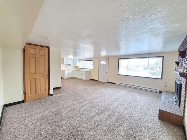 unfurnished living room featuring a brick fireplace, light colored carpet, a textured ceiling, sink, and baseboard heating