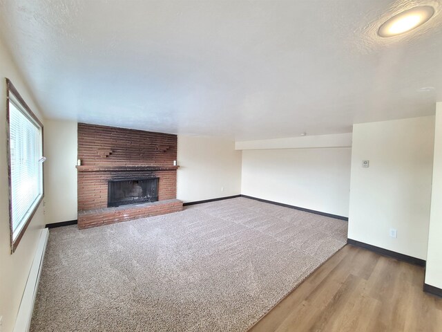 unfurnished living room featuring a fireplace, a baseboard radiator, and wood-type flooring