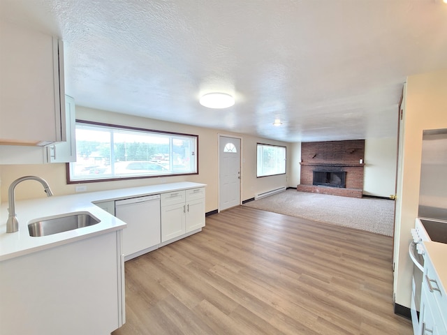 kitchen with white dishwasher, sink, a fireplace, white cabinetry, and light wood-type flooring