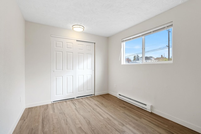 unfurnished bedroom featuring a closet, a textured ceiling, a baseboard radiator, and light wood-type flooring