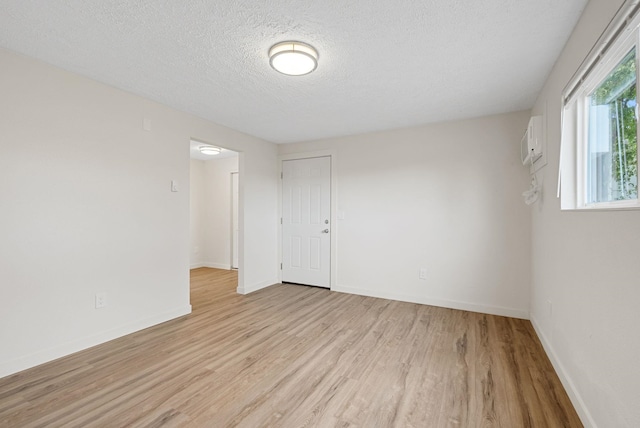 unfurnished room with a wall mounted air conditioner, a textured ceiling, and light hardwood / wood-style floors