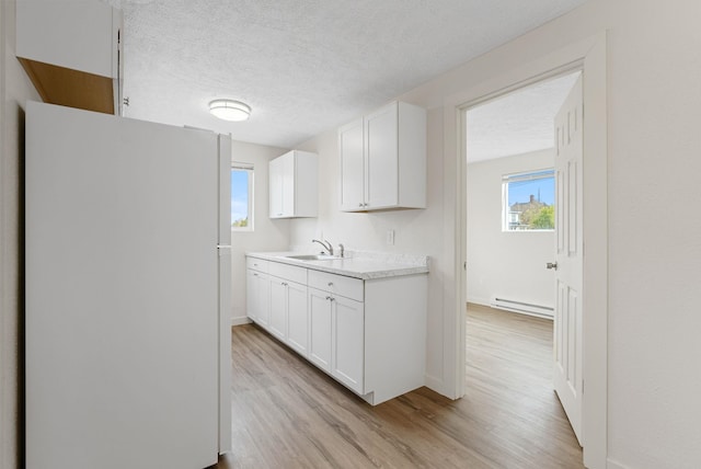 kitchen featuring sink, white cabinetry, baseboard heating, white fridge, and light hardwood / wood-style flooring