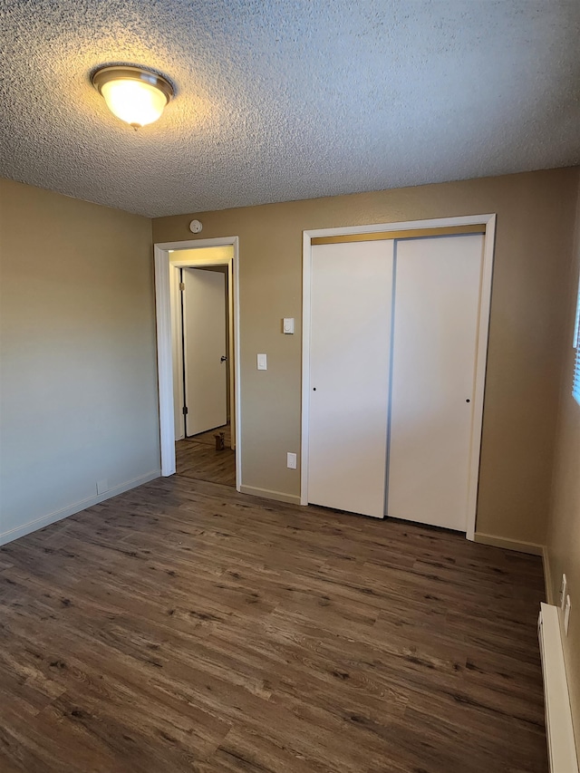 unfurnished bedroom with a closet, dark hardwood / wood-style floors, baseboard heating, and a textured ceiling