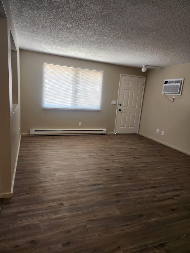 spare room featuring dark wood-type flooring, a baseboard heating unit, a wall mounted air conditioner, and a textured ceiling