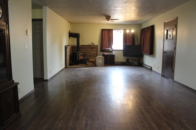 unfurnished living room featuring baseboard heating, a wood stove, a textured ceiling, a ceiling fan, and dark wood-style flooring