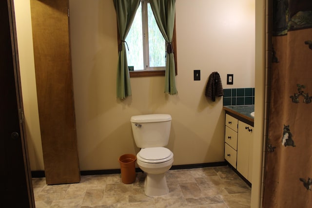 full bath with vanity, stone finish floor, toilet, and baseboards