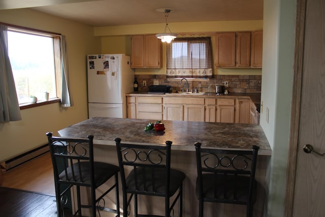 kitchen with a sink, light brown cabinets, a peninsula, freestanding refrigerator, and a baseboard radiator