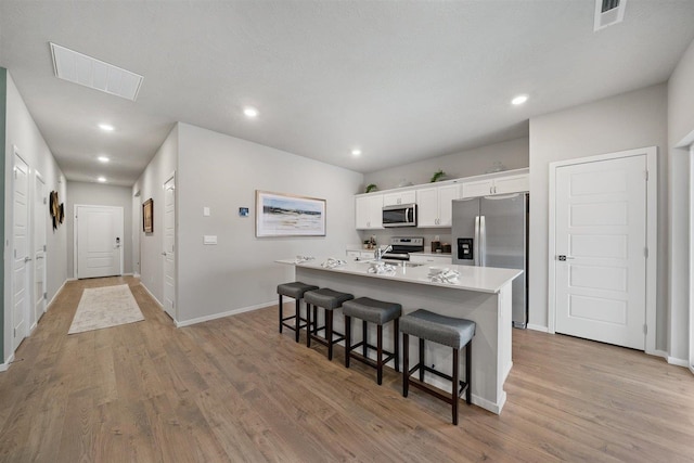 kitchen with white cabinets, a center island with sink, appliances with stainless steel finishes, a kitchen bar, and light wood-type flooring