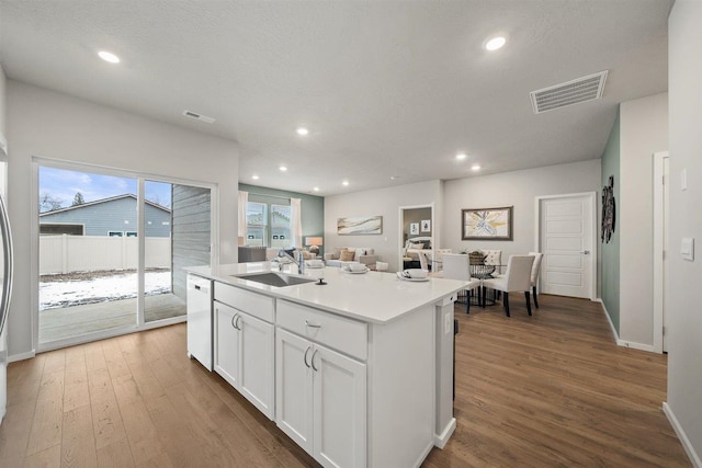 kitchen with an island with sink, white cabinetry, hardwood / wood-style flooring, white dishwasher, and sink