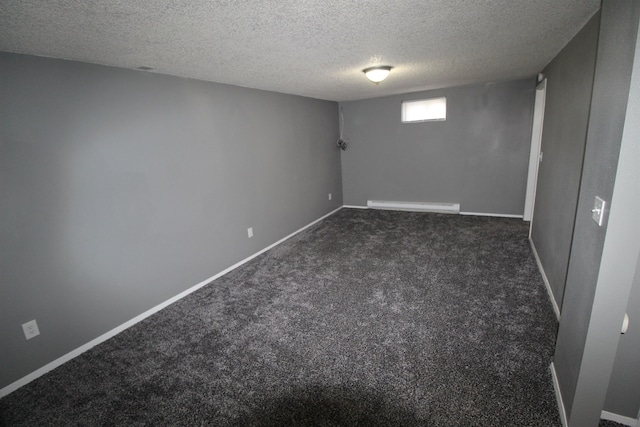 basement with a textured ceiling, a baseboard heating unit, and dark carpet