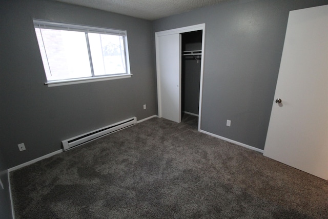 unfurnished bedroom featuring a closet, a baseboard heating unit, a textured ceiling, and dark colored carpet